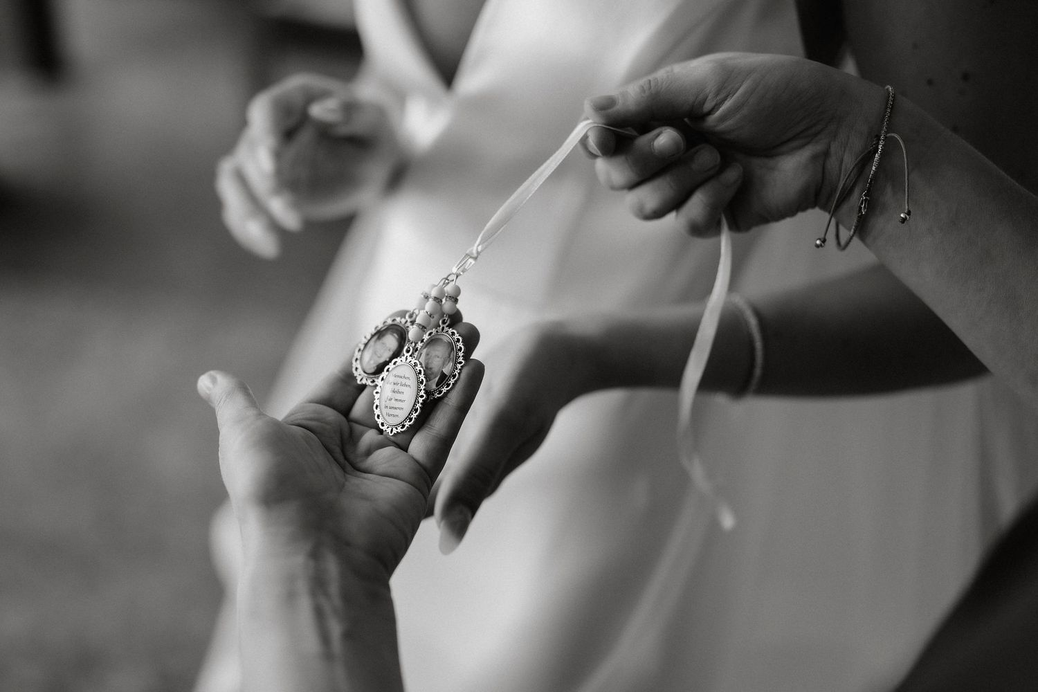 Black and white detail shot of hands helping with wedding dress and jewelry preparations.