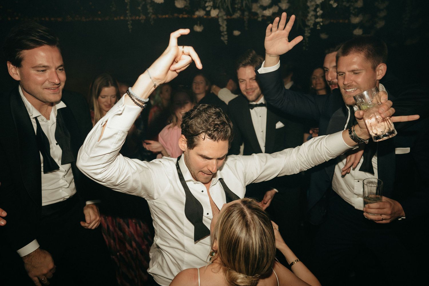 People dancing and celebrating at a lively wedding reception party with drinks in hand.