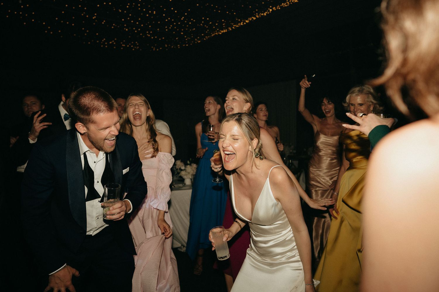 Wedding guests dancing and celebrating on a dance floor at an evening reception.