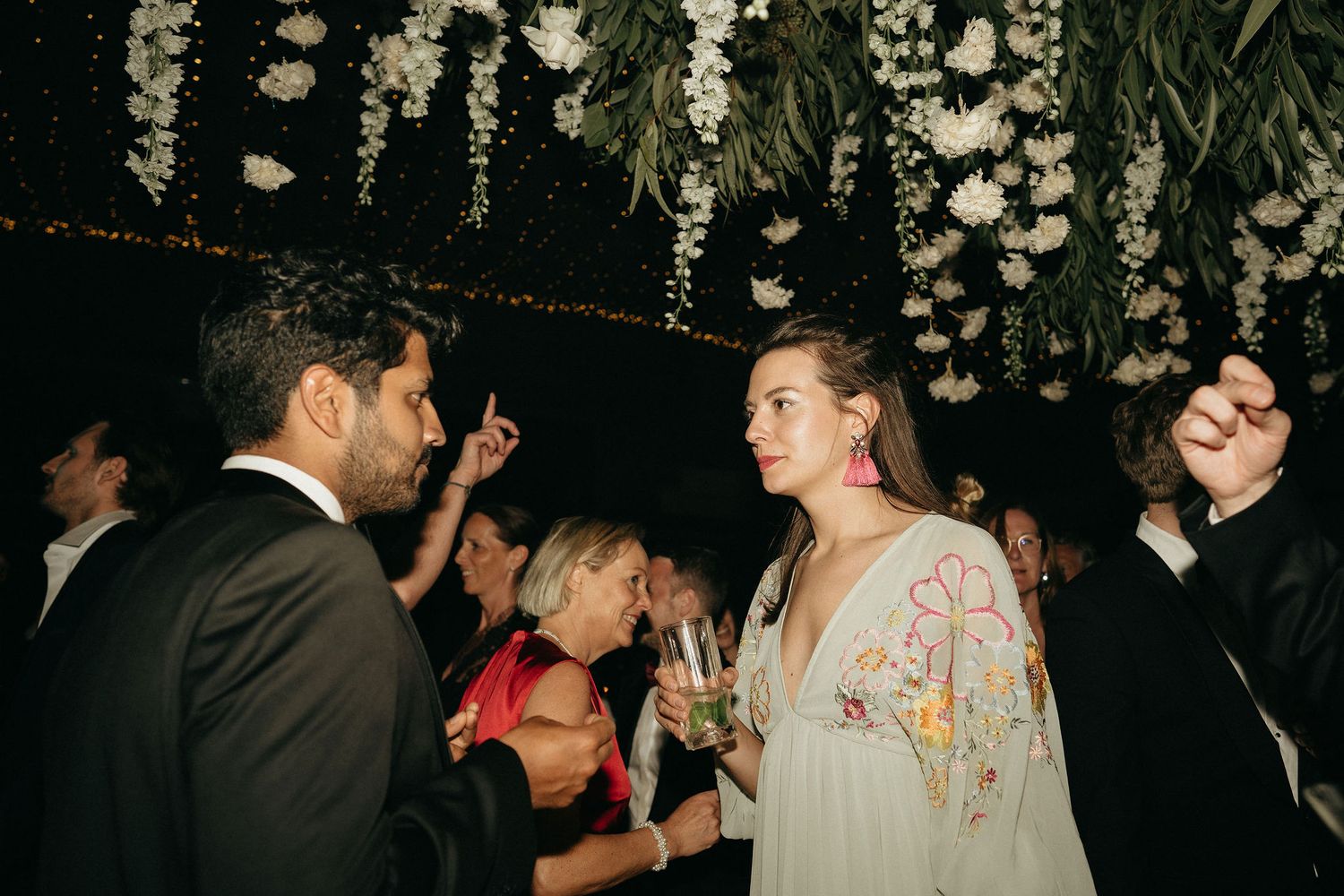 A couple shares a romantic dance moment at an evening wedding reception under decorative string lights.