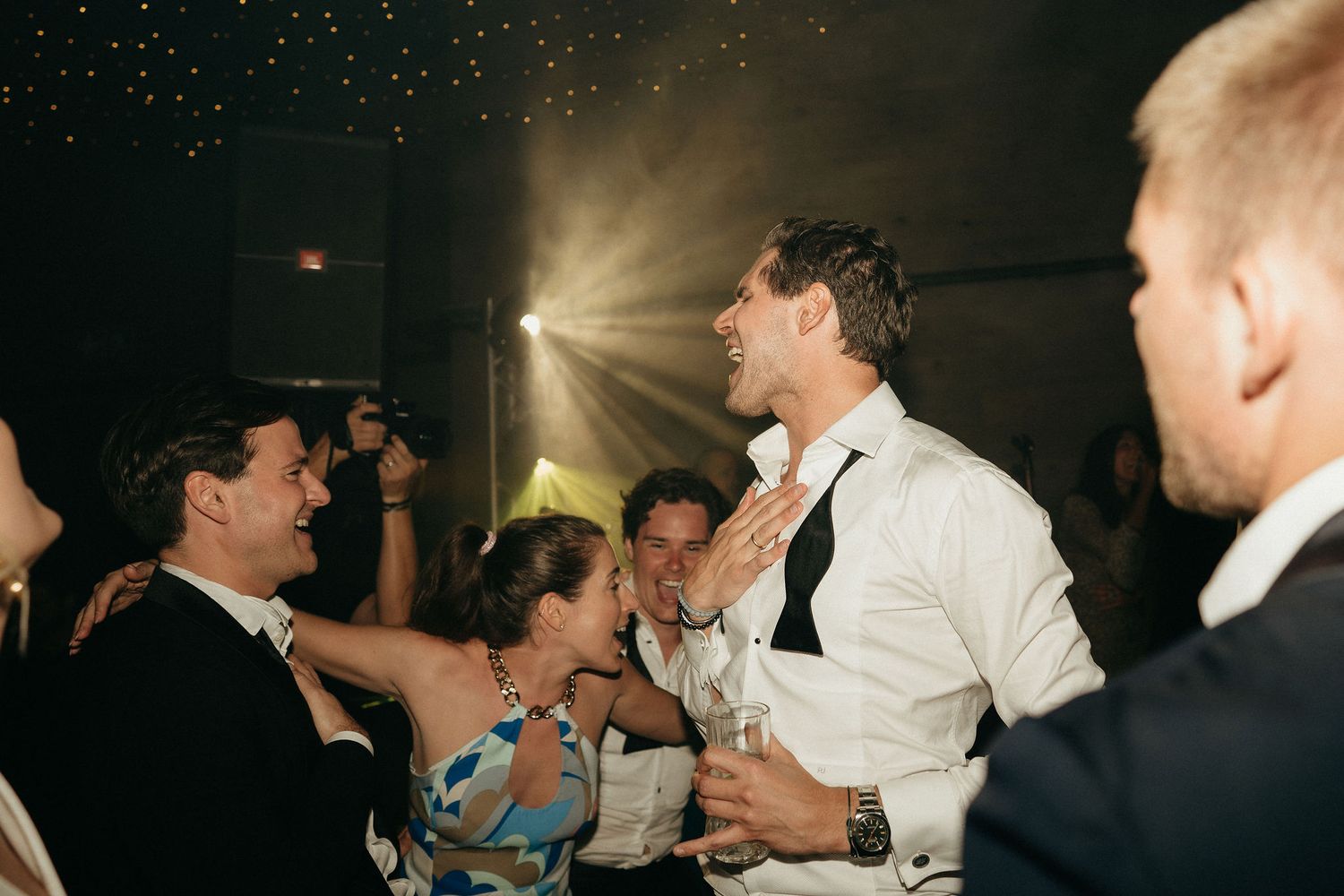 People dancing and celebrating at a dimly lit wedding reception party on the dance floor.