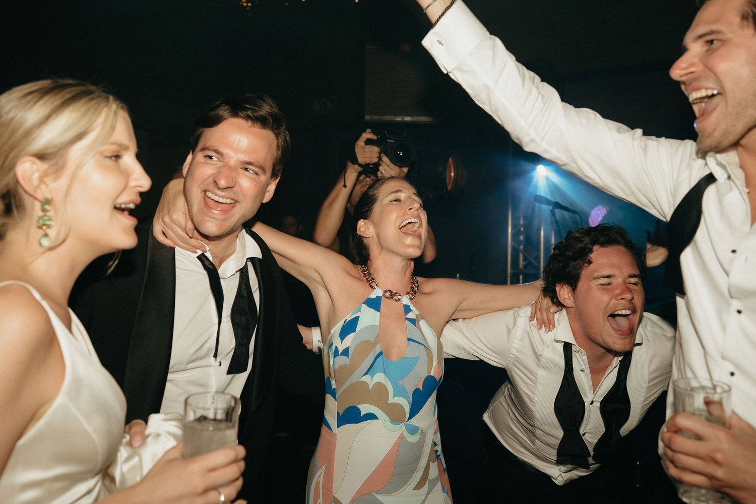 A group of wedding guests dancing and laughing together on the dance floor at a reception celebration.