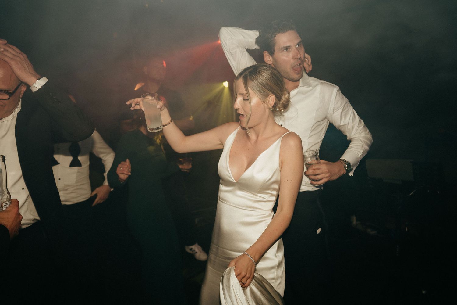 Wedding guests dancing together on a dark dance floor with atmospheric lighting.
