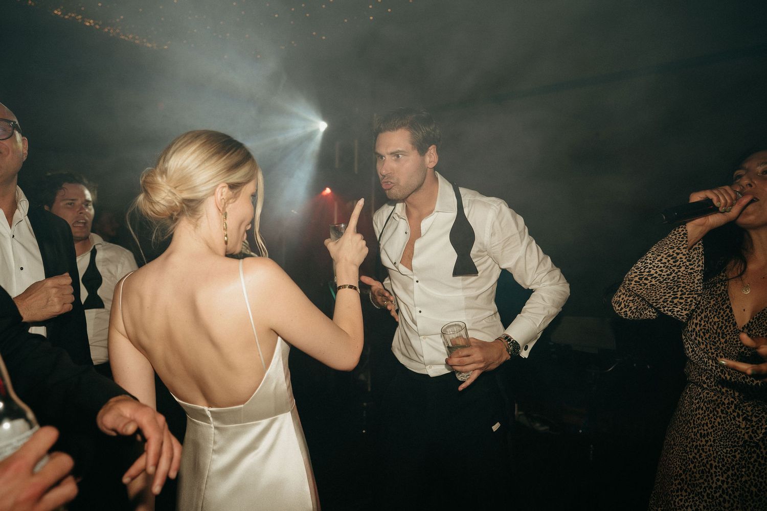 People dancing and celebrating at a wedding reception in a dimly lit venue.