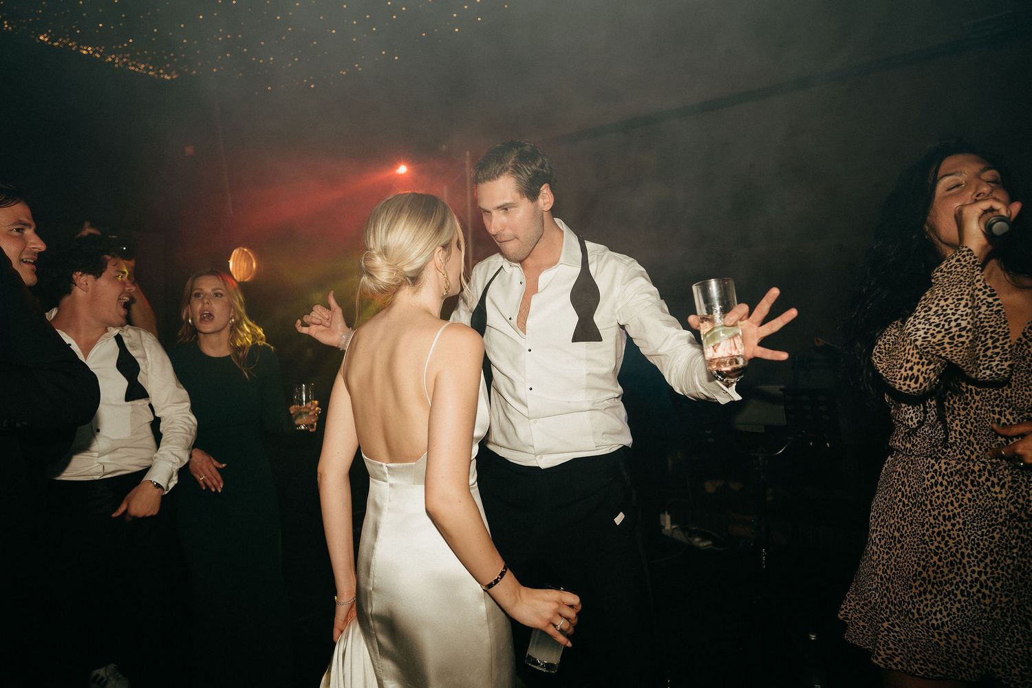 People dancing together in a dimly lit room during what appears to be a wedding reception or party celebration.