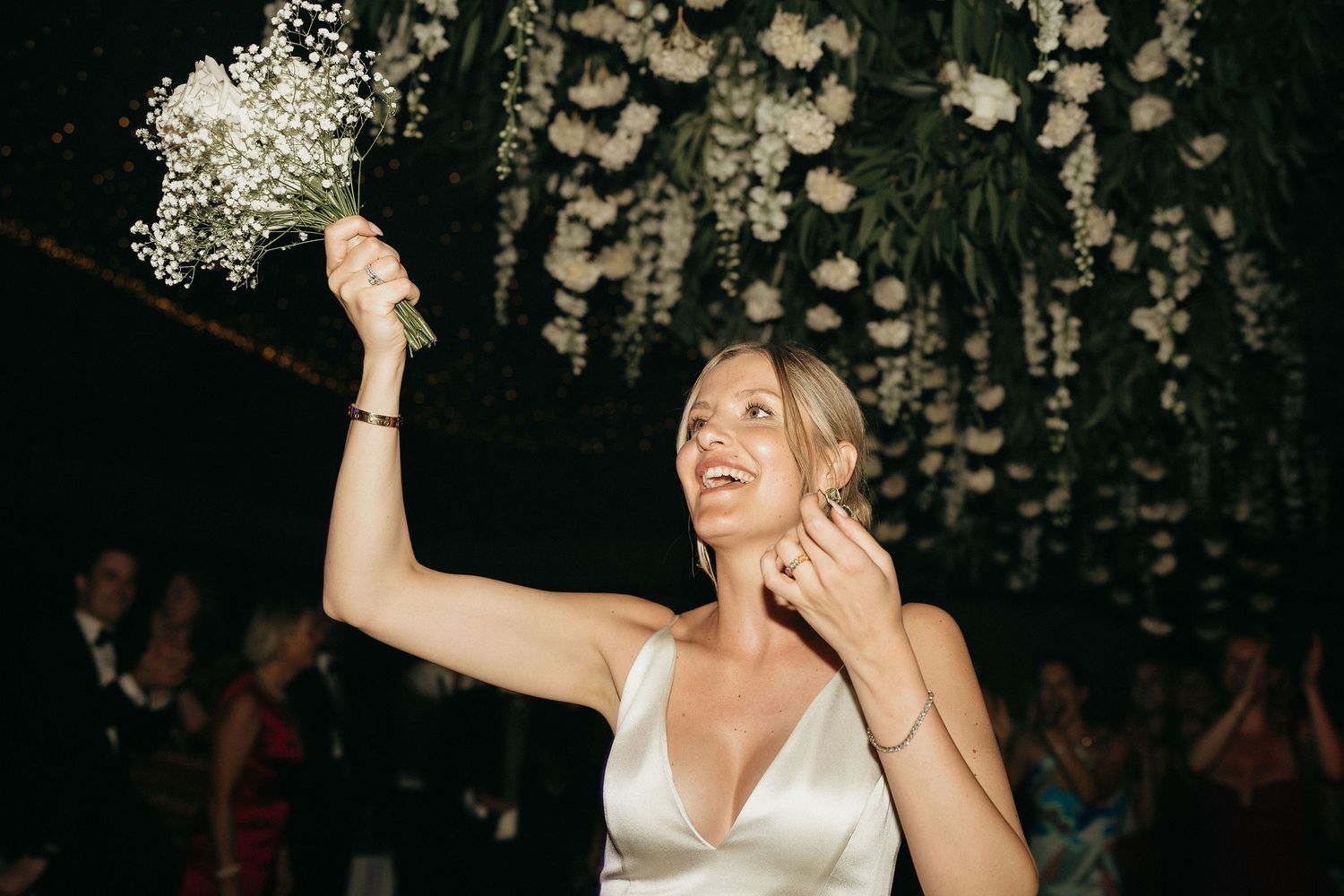 A couple dances joyfully beneath a ceiling decorated with hanging lights and floral arrangements at a wedding reception.