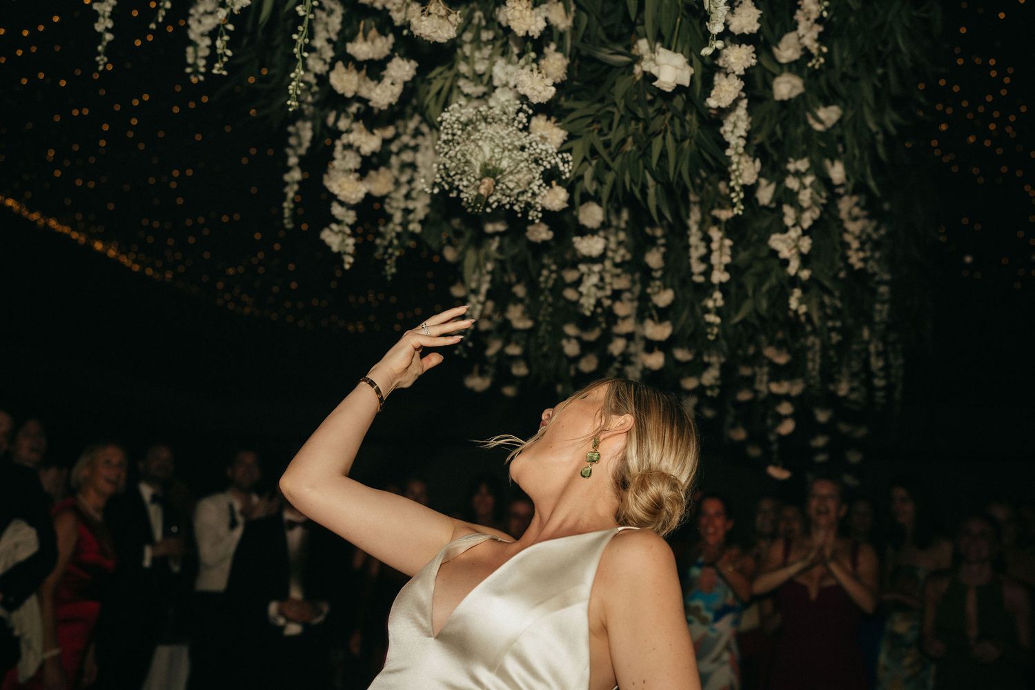 Couple dancing together at a wedding reception under hanging floral decorations and string lights.