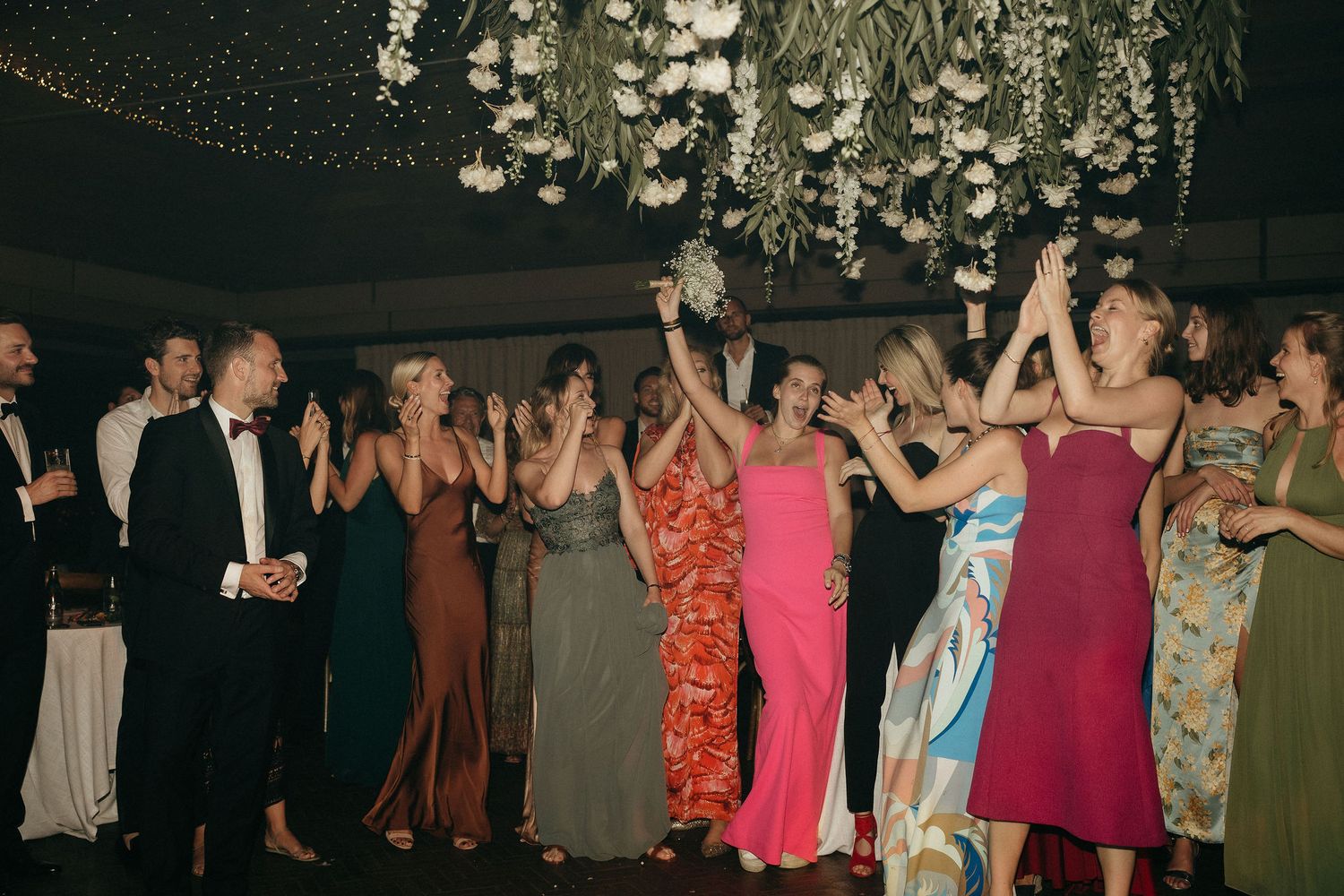 People dancing together at a formal event under decorative lighting in an indoor venue.