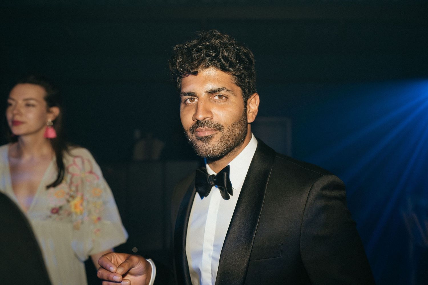 A group of people in formal attire gather at an elegant evening event with blue lighting.