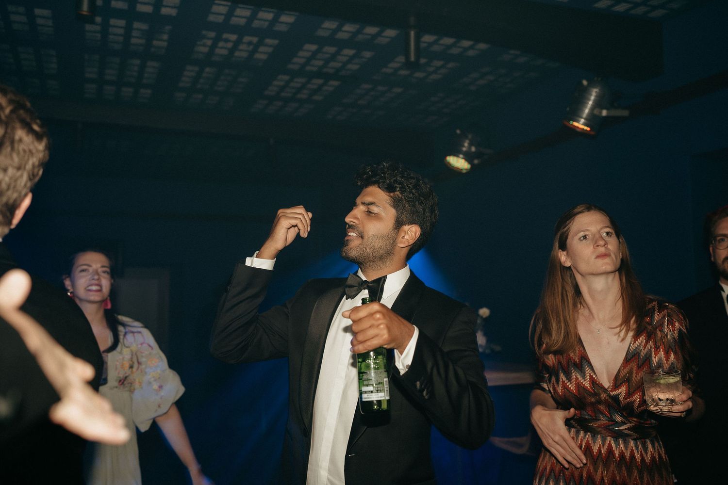 People dancing and socializing at a dimly lit party venue with blue lighting and festive atmosphere.