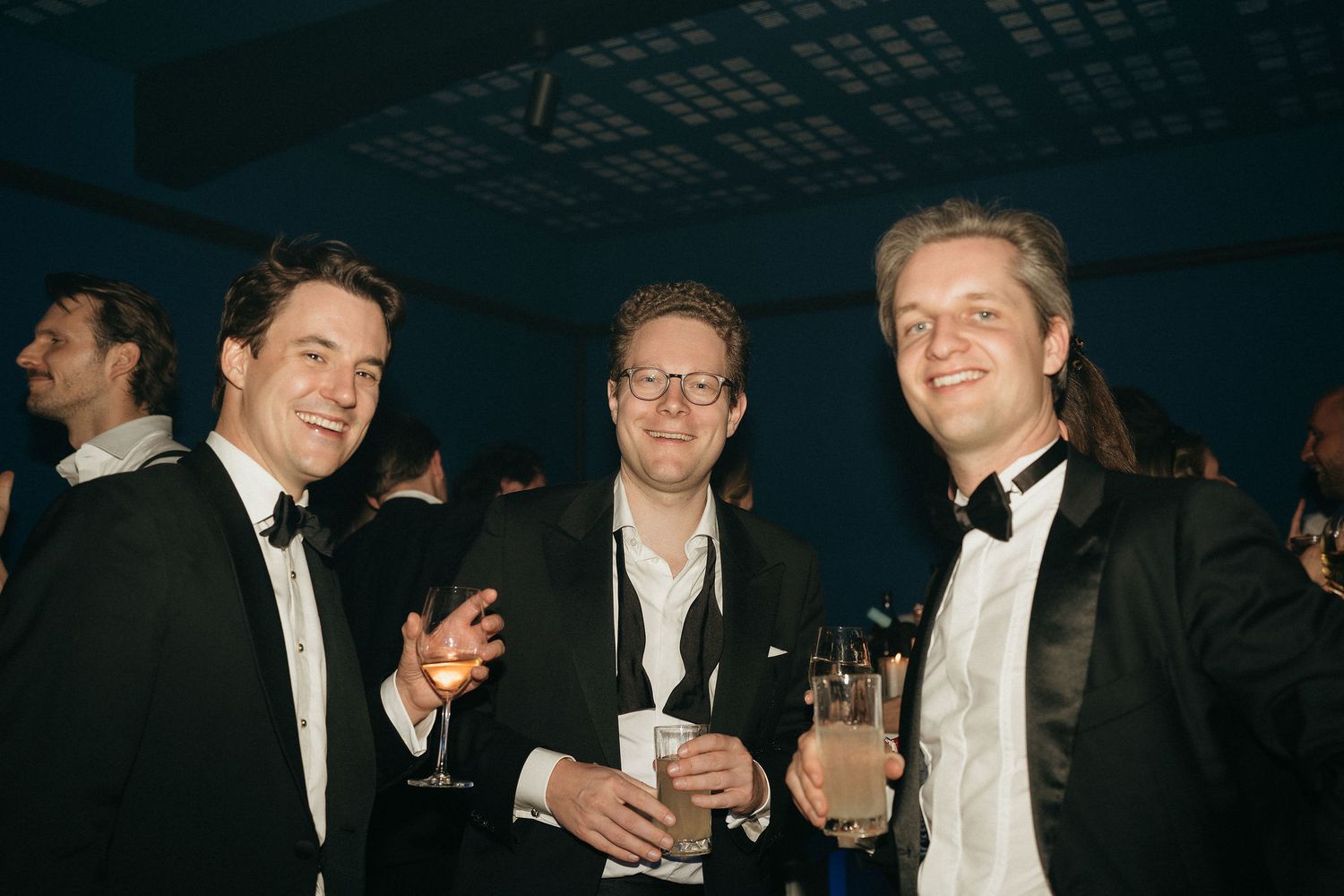 Guests in formal black tie attire socialize and laugh together at an elegant evening event.