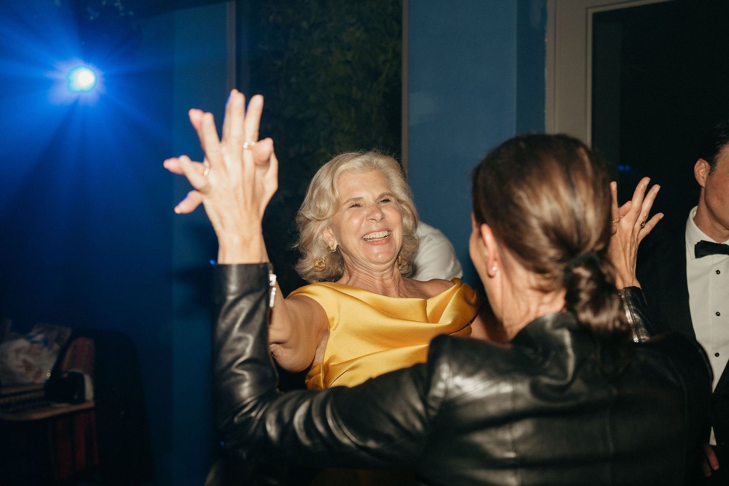 People dancing and celebrating with raised hands in a dark nightclub setting illuminated by blue lighting.