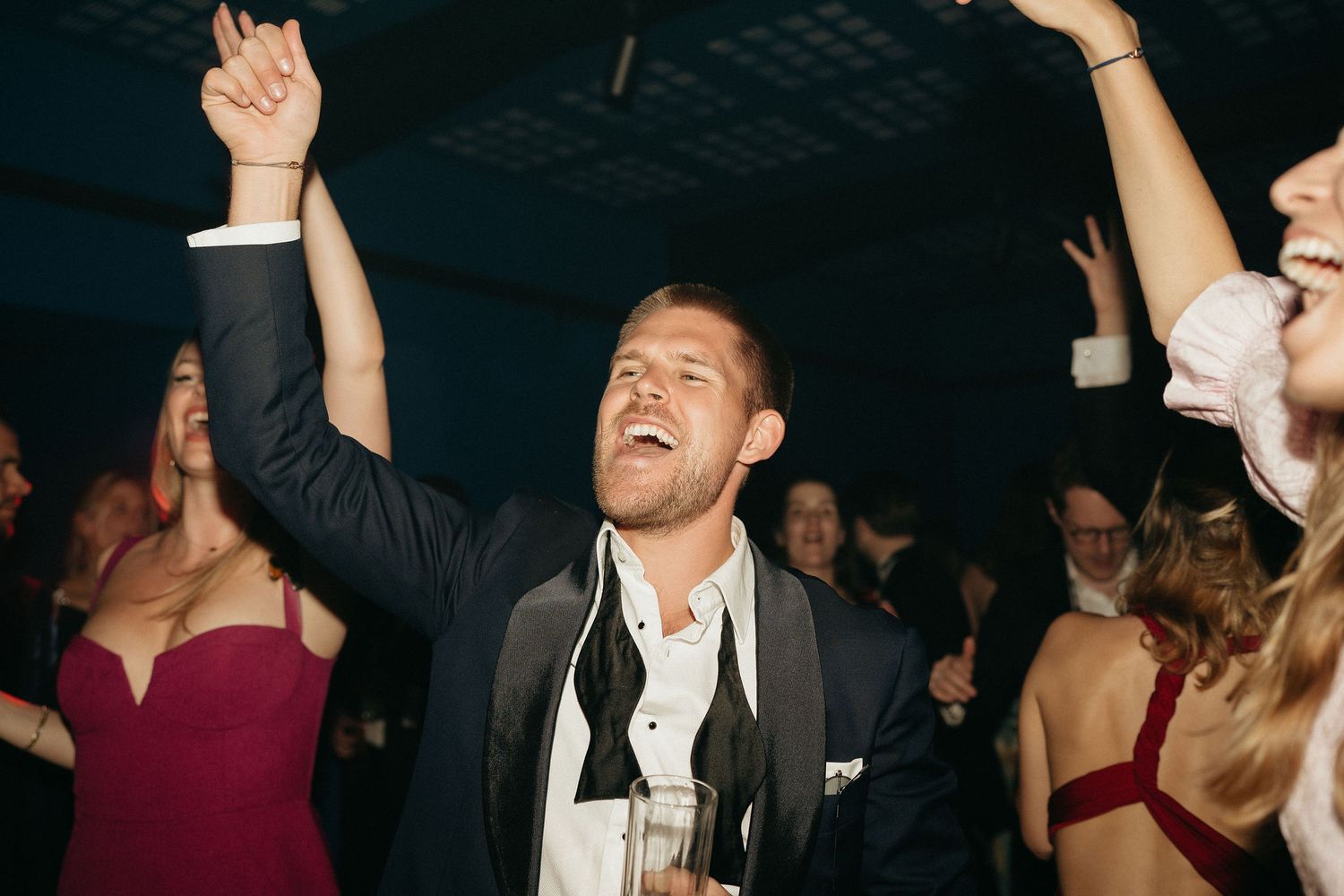 A group of people dancing and celebrating at a lively party with raised arms and joyful expressions.