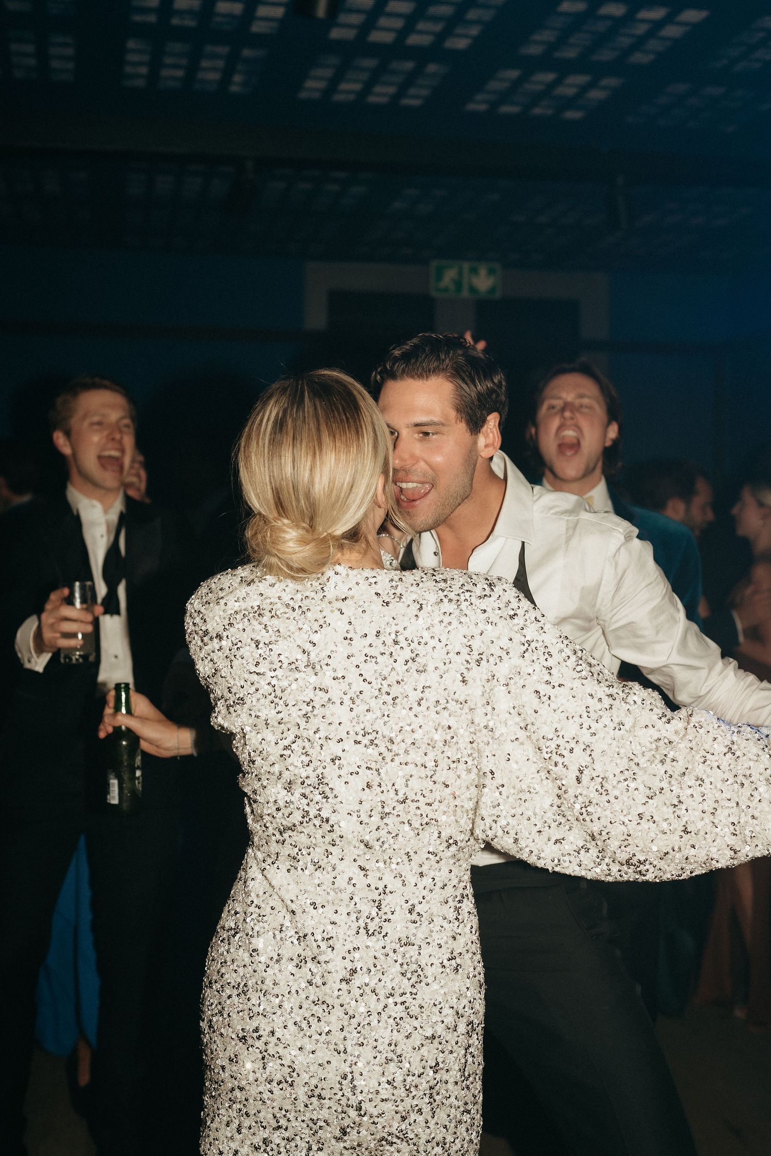 A couple dances together at a dimly lit party venue with others visible in the background.