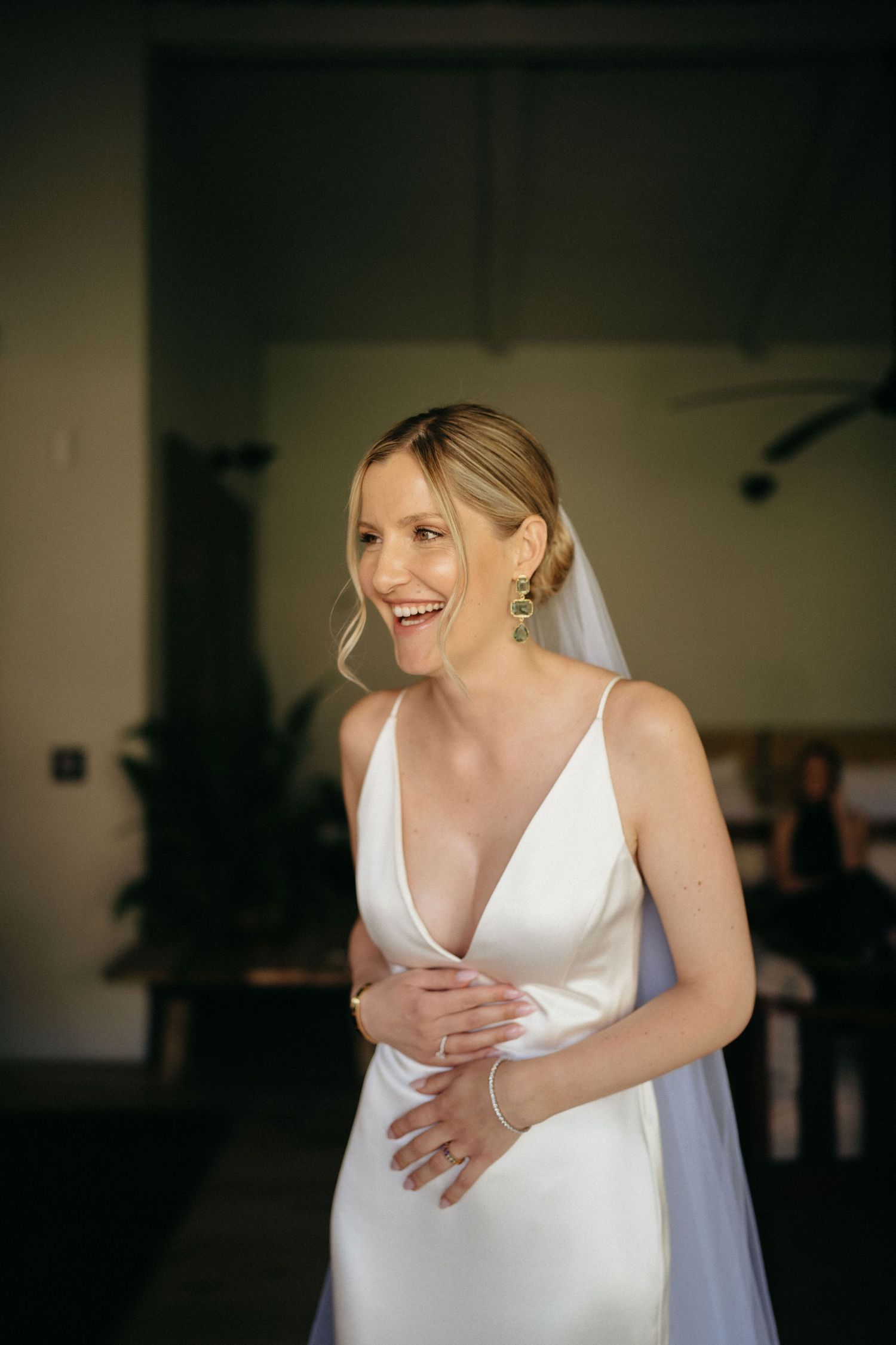 A bride in a white wedding dress laughs joyfully while holding her stomach in a candid moment.