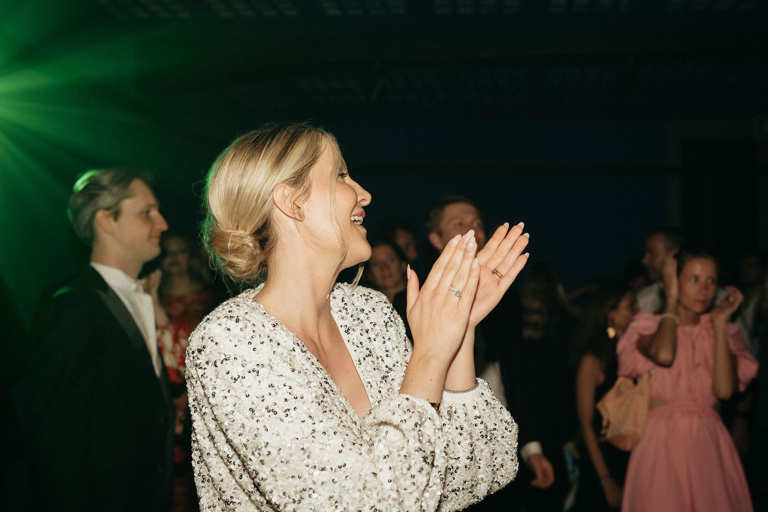 Wedding guests dancing together on a dark dance floor illuminated by green lighting.