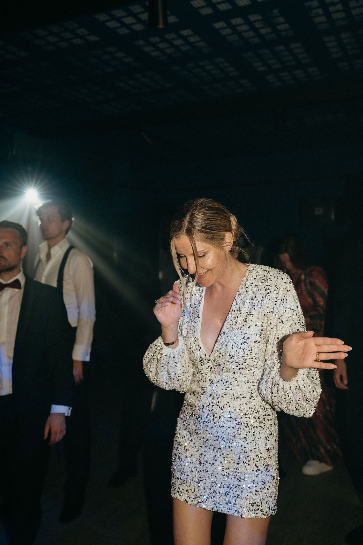 Person in a sparkly white top dances energetically on a dark dance floor at a formal event.