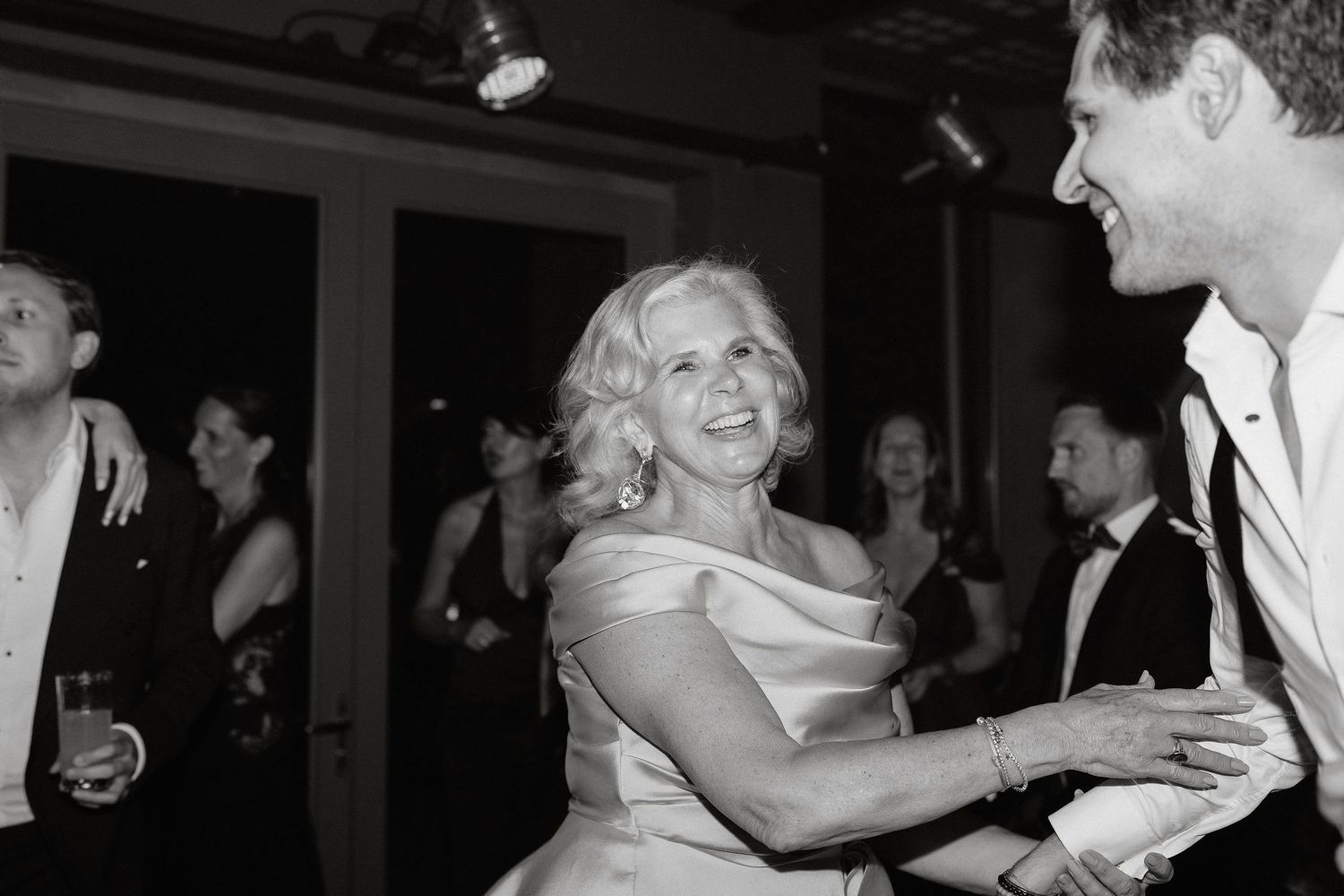 A black and white photo shows a couple dancing together at a wedding reception with other guests in the background.
