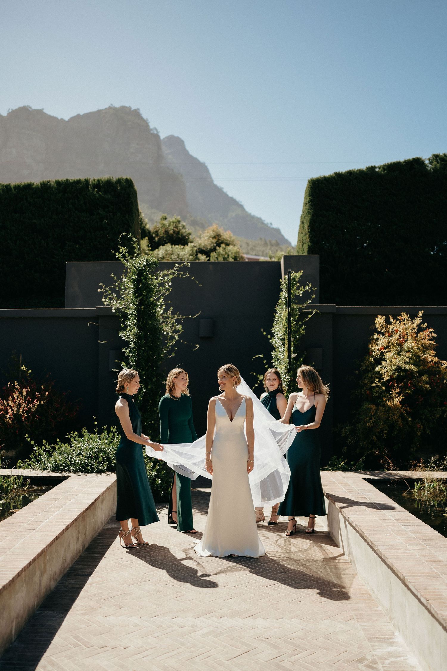 Group in formal attire posing on a sunny terrace with mountain views in the background.