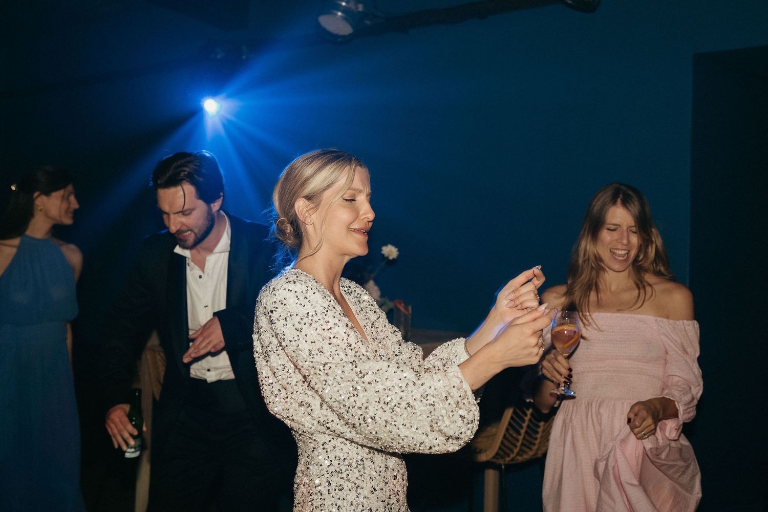 People dancing together on a dark dance floor with blue lighting at what appears to be a wedding reception or party.