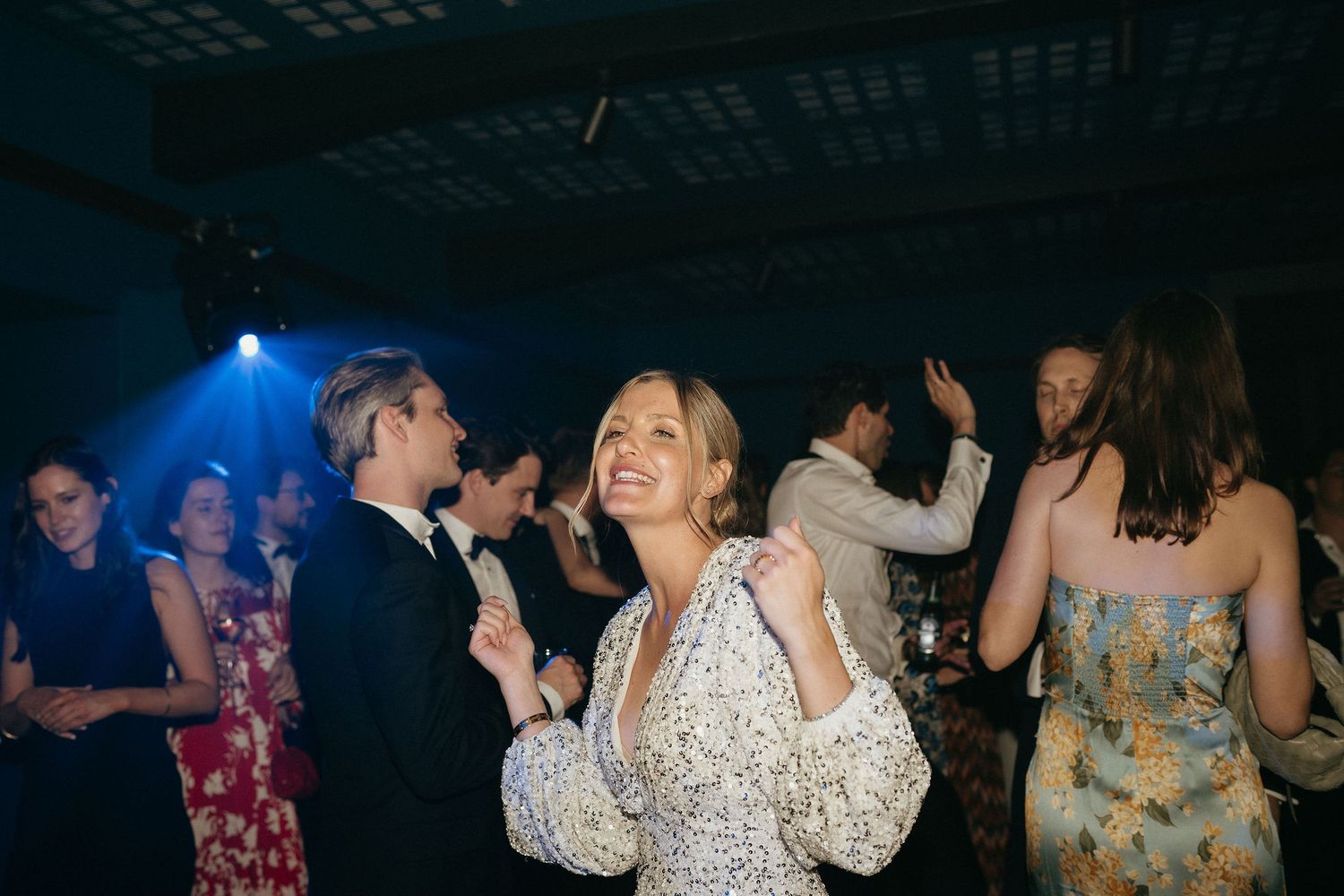 People dancing and socializing at a dimly lit nightclub or party venue with blue lighting effects.