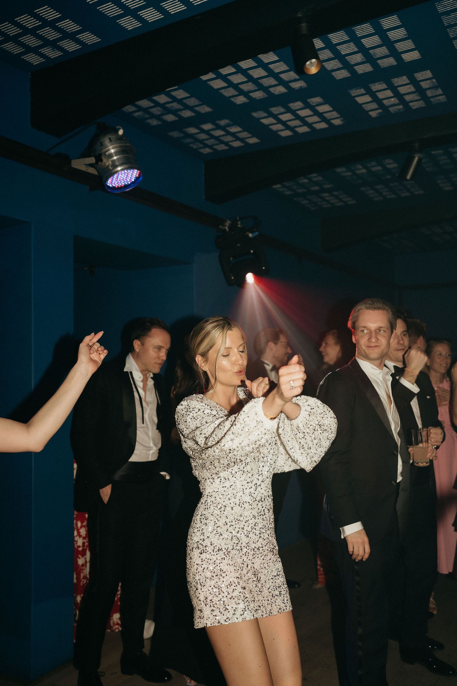 People dancing and socializing at a dimly lit party venue with an illuminated ceiling grid.