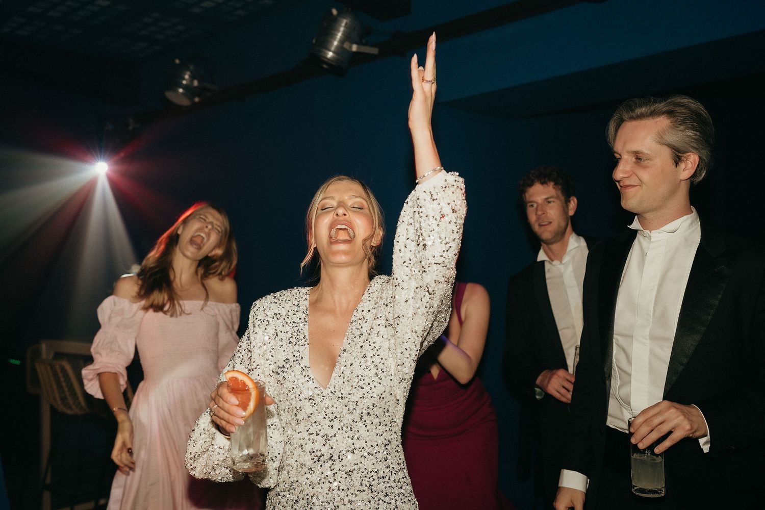 A group of people dancing and celebrating at a dimly lit party venue with dramatic lighting effects.