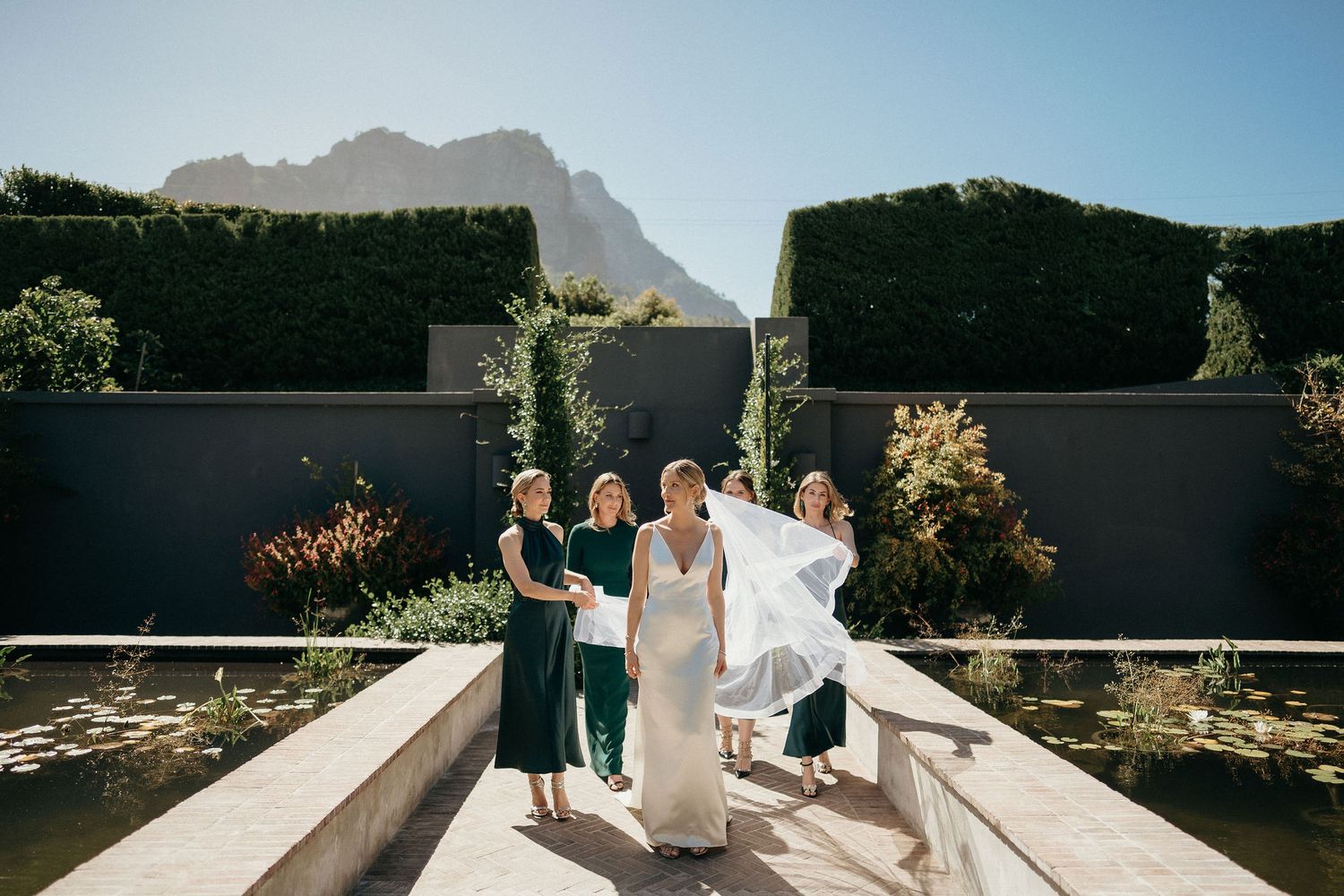 A couple in wedding attire embraces on a deck overlooking scenic mountain landscapes during a sunny day.