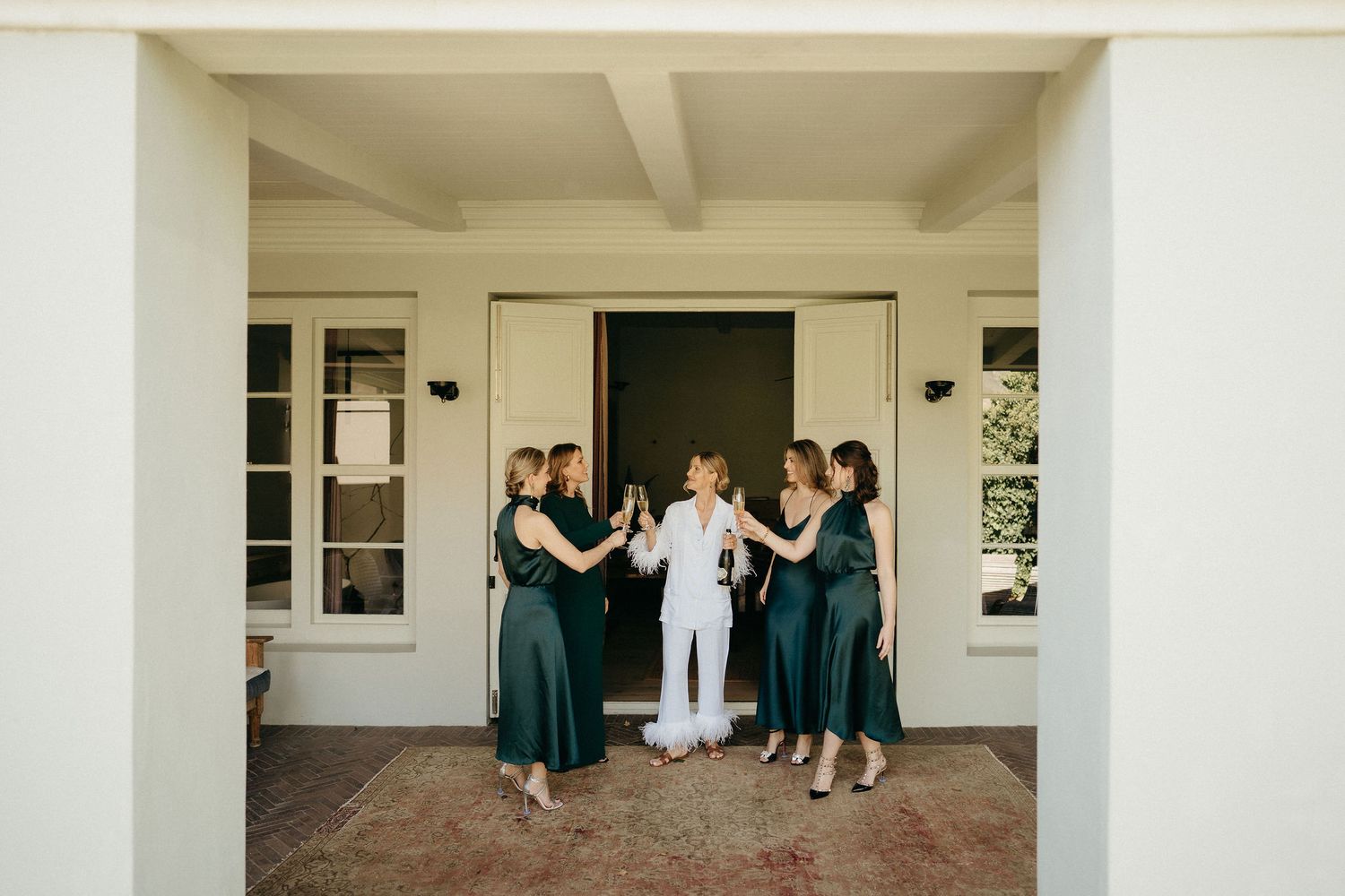 A group in formal attire stands together on a covered porch of a white building during a special event.