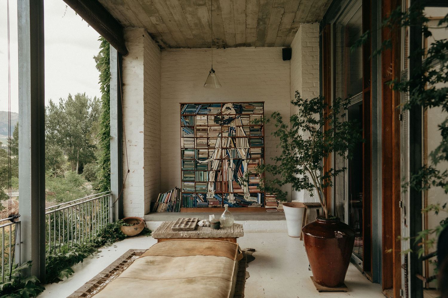Long concrete corridor with windows and potted plants leading to a bright outdoor area.