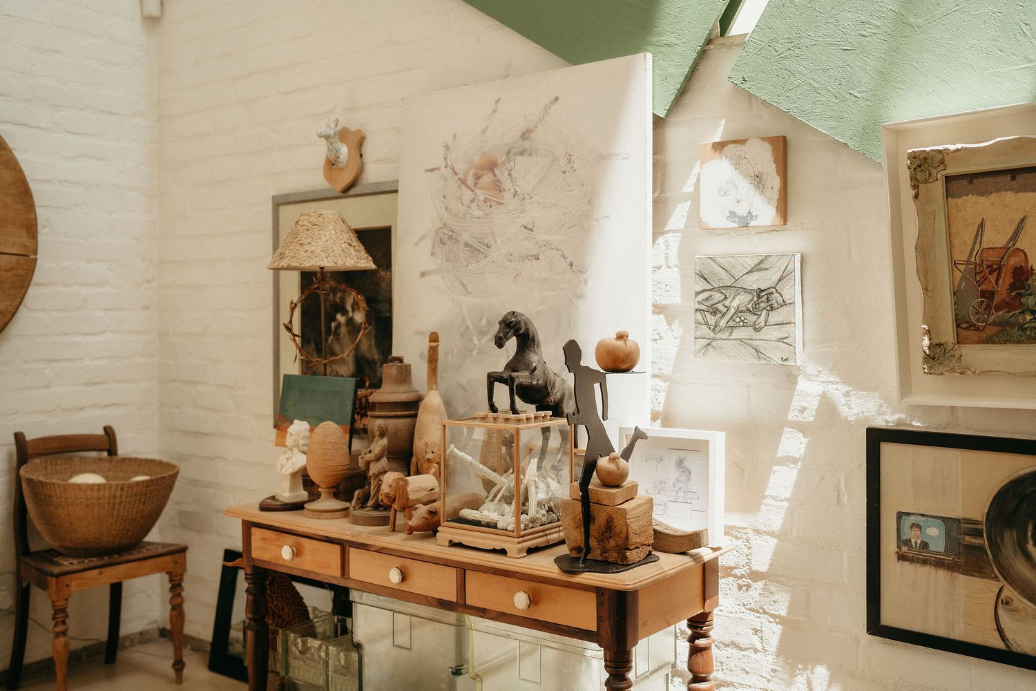 Rustic wooden table displays vintage decor items and antiques in a sunlit room with white brick walls.