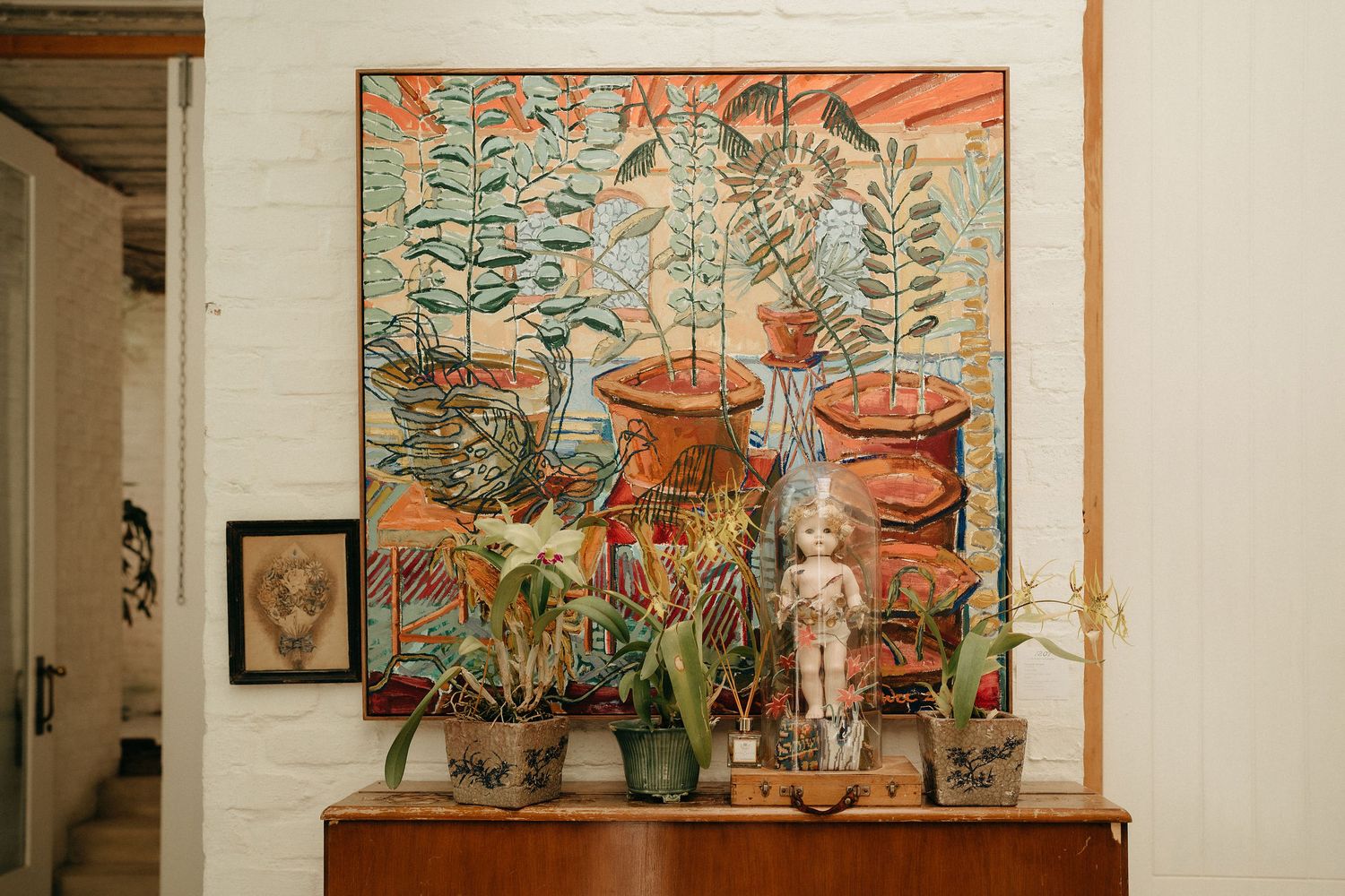 A gallery wall displays colorful botanical artwork alongside decorative terracotta pots on wooden shelving.