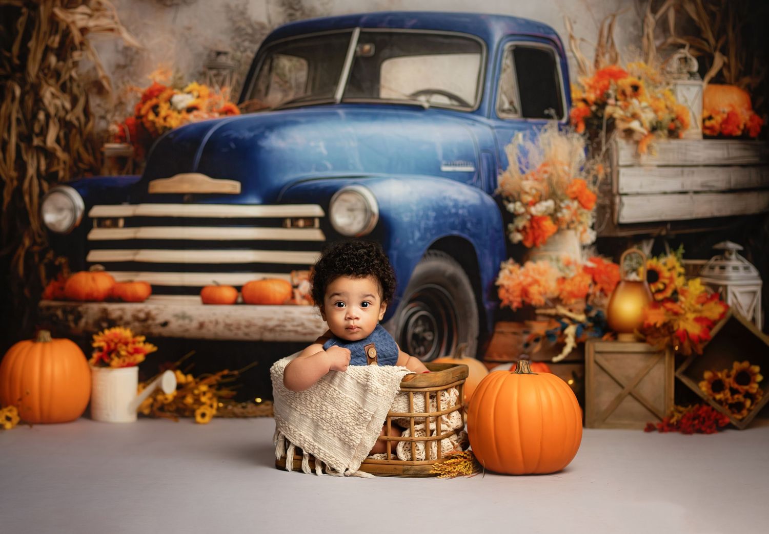 Fall themed photo setup with vintage blue truck, pumpkins, and autumn decorations in warm rustic setting.