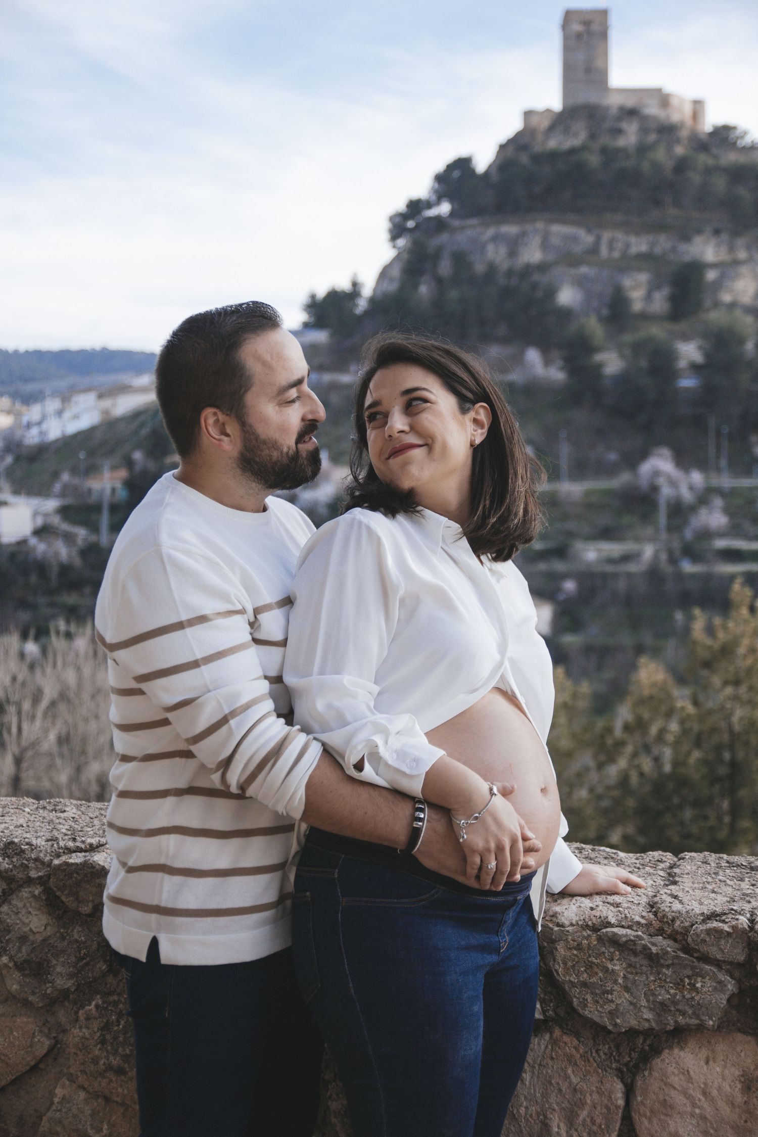 Romantic couple embracing on stone wall with scenic mountain village backdrop.