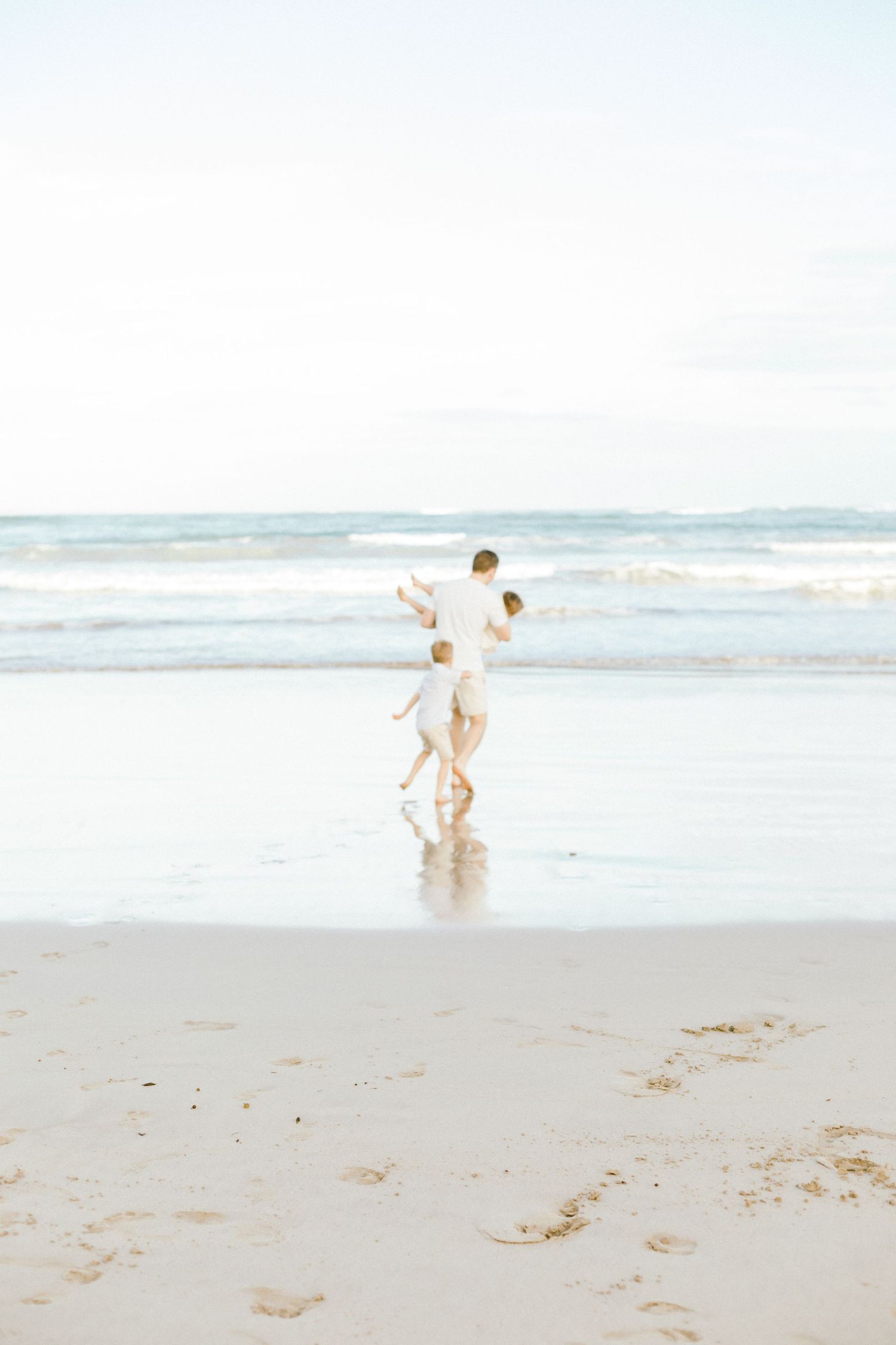 Two people in white outfits playing and splashing together on a serene beach with ocean waves in the background.