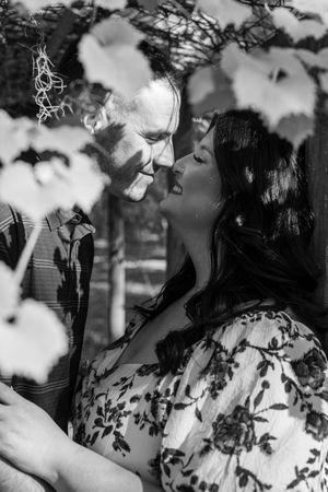 Black and white photo of a romantic couple sharing an intimate moment surrounded by lush foliage.