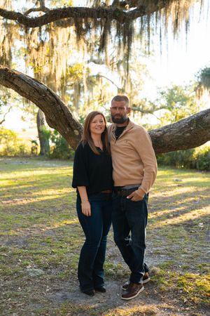 Couple sharing a playful moment under a large oak tree with Spanish moss.