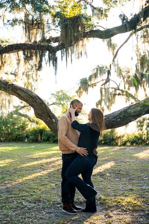 Couple posing together under a dramatic Spanish moss-covered tree at sunset.
