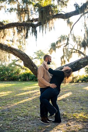 A couple dances playfully under Spanish moss draped oak trees in a romantic outdoor setting.