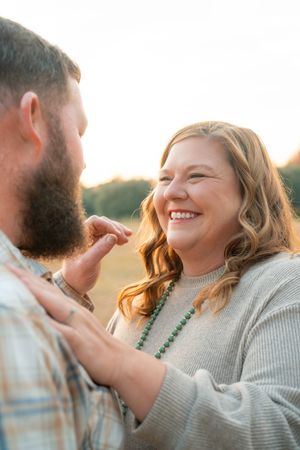 A couple shares a tender moment of laughter and joy together during golden hour in a field.