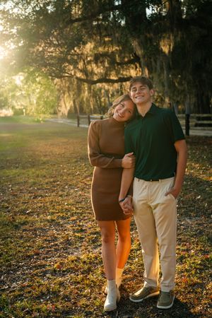 Couple walking together through a sunlit park with autumn leaves scattered on the ground during golden hour.