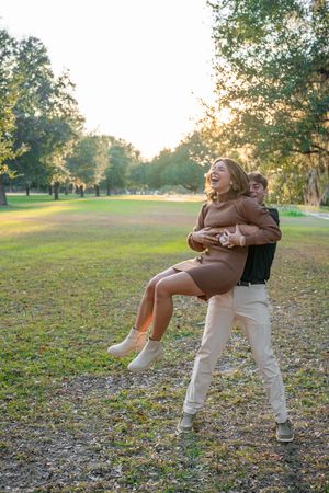 A playful couple embraces while spinning in a park with fallen autumn leaves during golden hour sunset.