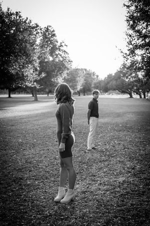 Two people walk together across a grassy field in black and white, creating a serene silhouette against nature.