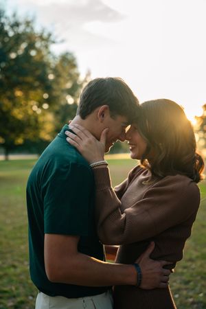 Intimate couple sharing tender moments in a park backlit by warm sunset light filtering through trees.