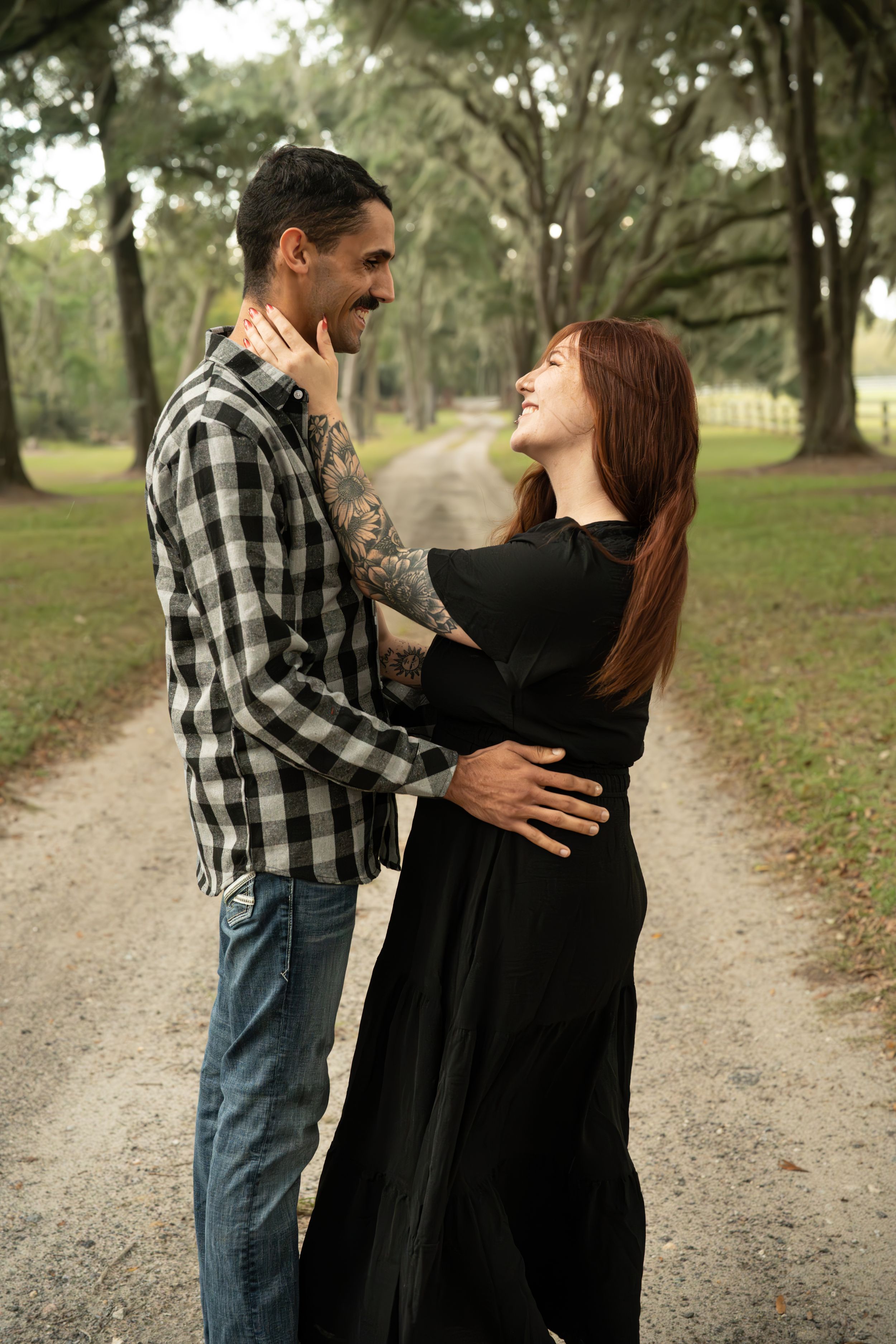 Romantic couple embracing on a tree-lined path in casual attire.