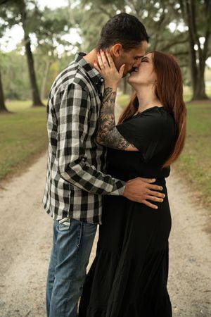 Romantic couple embracing on a scenic dirt path surrounded by trees.