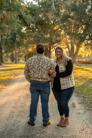 Couple walking together on a scenic gravel path during sunset at a rustic venue.