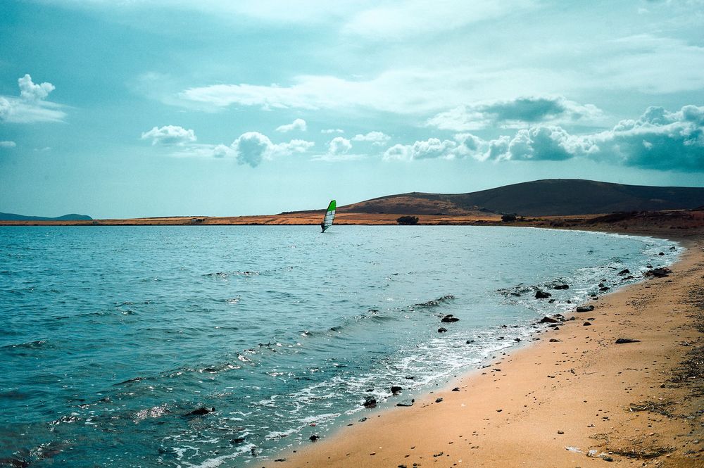 A scenic coastal landscape with sandy beach, scattered rocks, and blue waters stretching to the horizon.