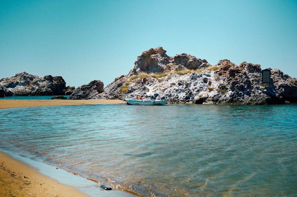 Panoramic view of a rocky coastline with crystal clear turquoise waters and sandy beach under bright blue skies.