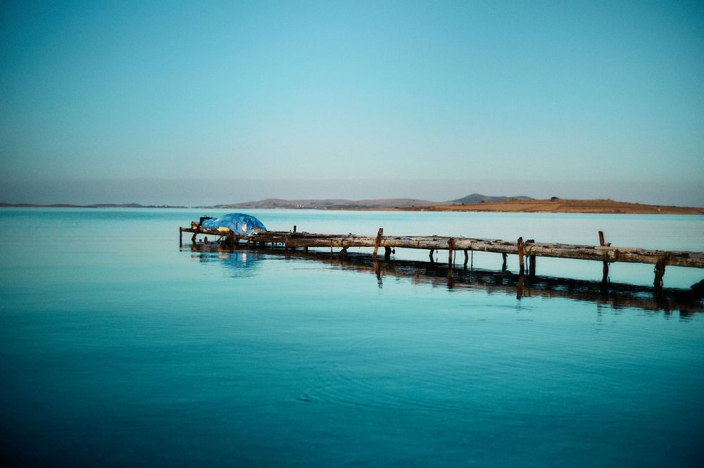 Tranquil blue seascape with wooden pier extending into calm waters under bright sky.